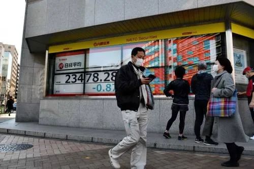 ▲2月21日,在日本东京,路人走过街边的电子股指信息显示屏。(新华社/法新)